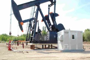 Industrial natural gas compressor unit operating beside an oil pumpjack at an energy production site, illustrating common types of natural gas compressors used in oil and gas operations.