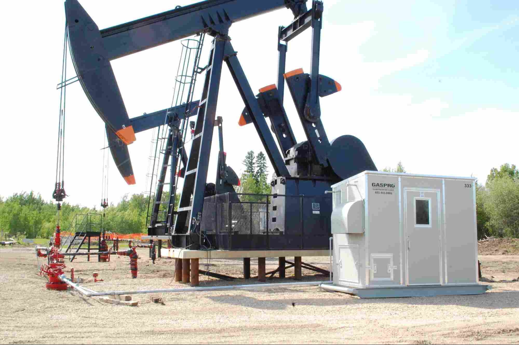 Industrial natural gas compressor unit operating beside an oil pumpjack at an energy production site, illustrating common types of natural gas compressors used in oil and gas operations.